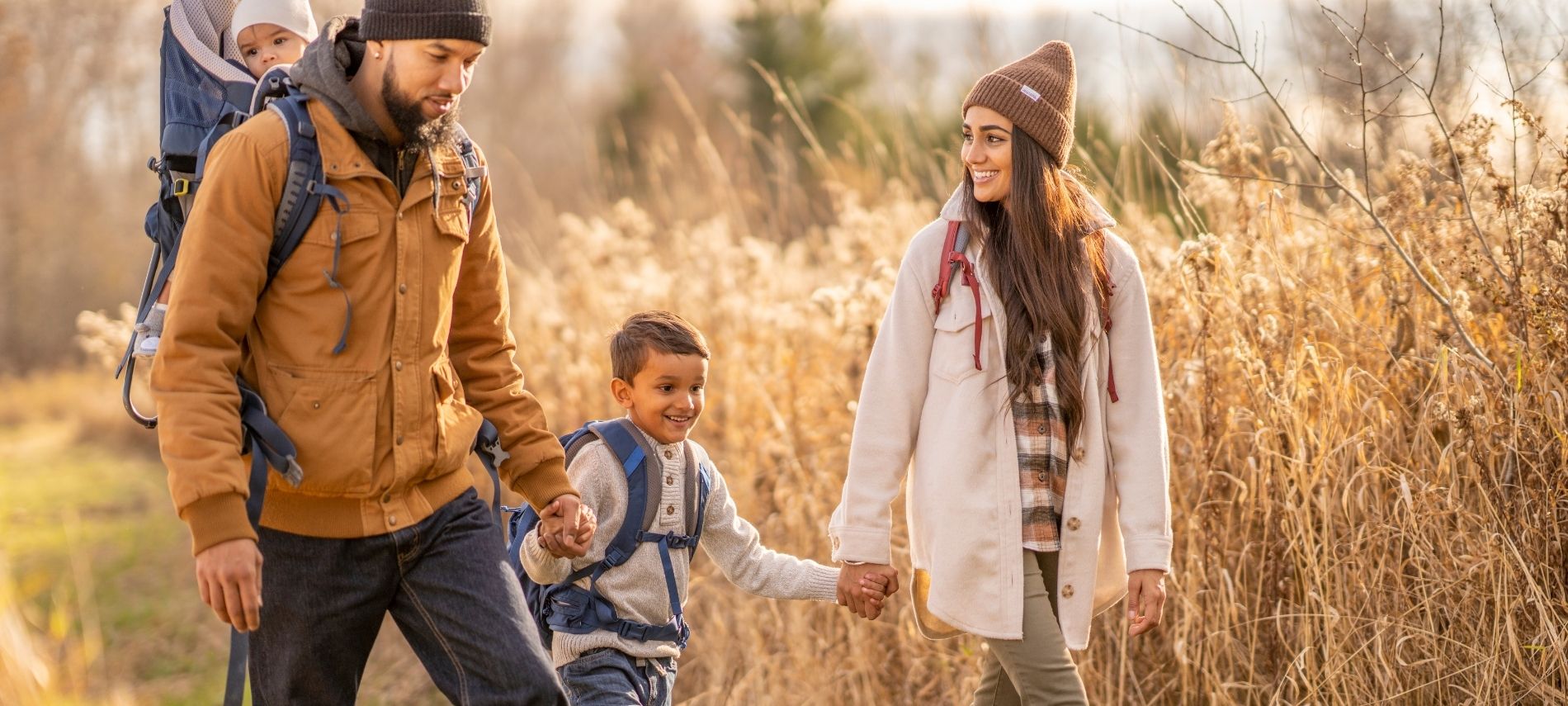 a family holding hands while going on a walk in autumn next to dried plant stalks