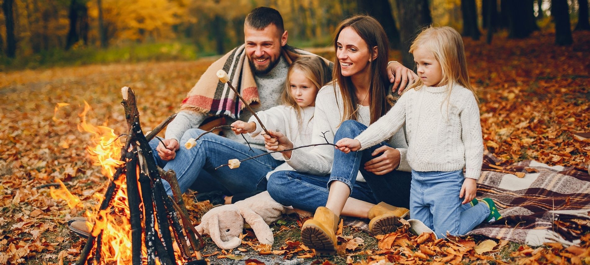 family with kids roasting smores in autumn forest