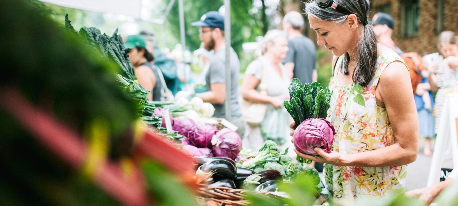 a woman is holding cabbage and kale while shopping at a farmers market